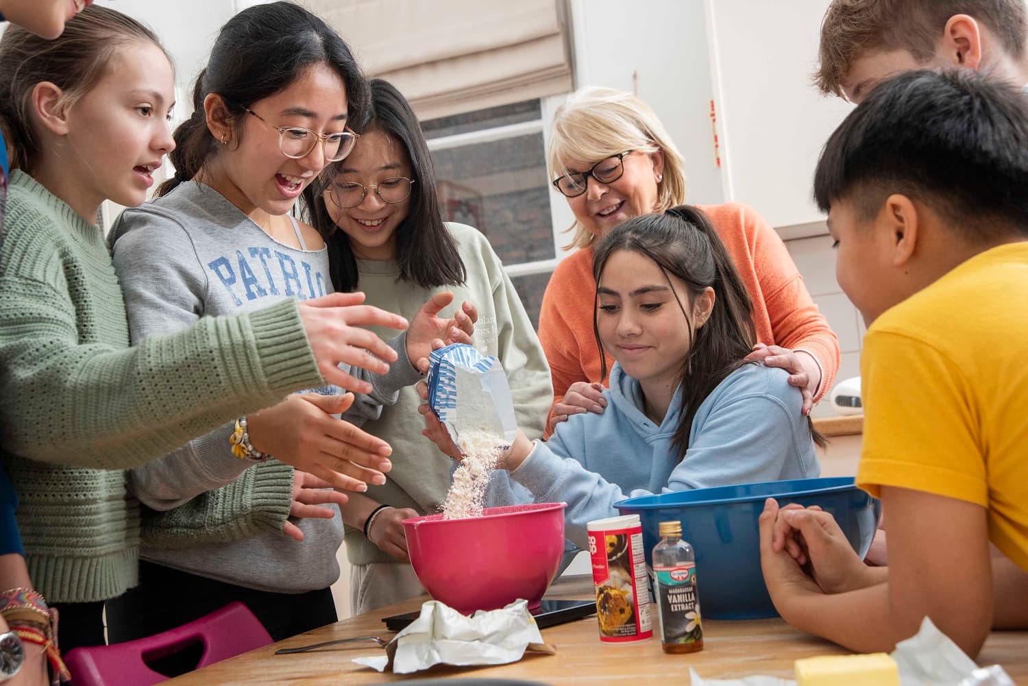 A group of people, including a woman and children, joyfully baking together in a kitchen, with bowls and ingredients on the table.