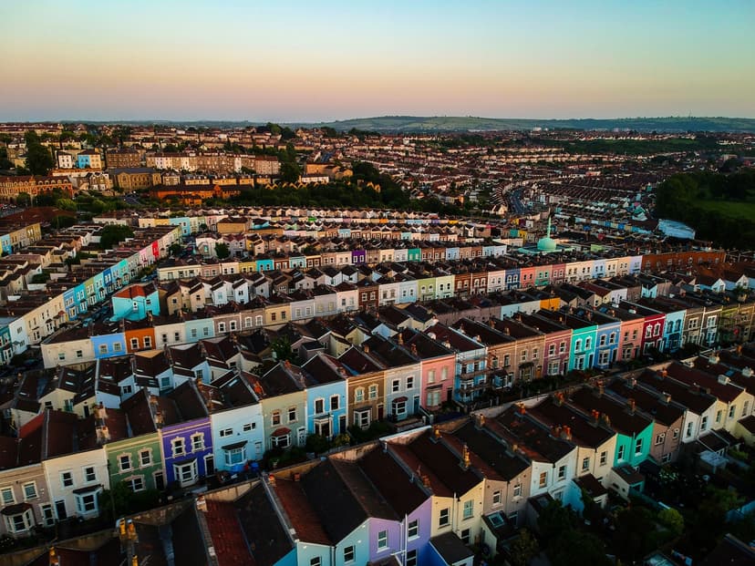 Aerial view of a colorful row of houses in a densely packed neighborhood at sunset, with rolling hills in the background.