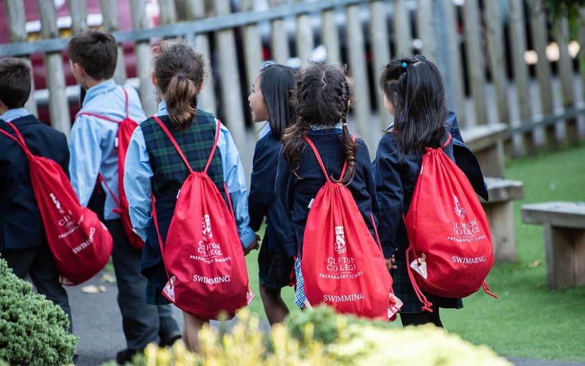 Children in school uniforms walking together outdoors, each carrying a red drawstring bag with white text.