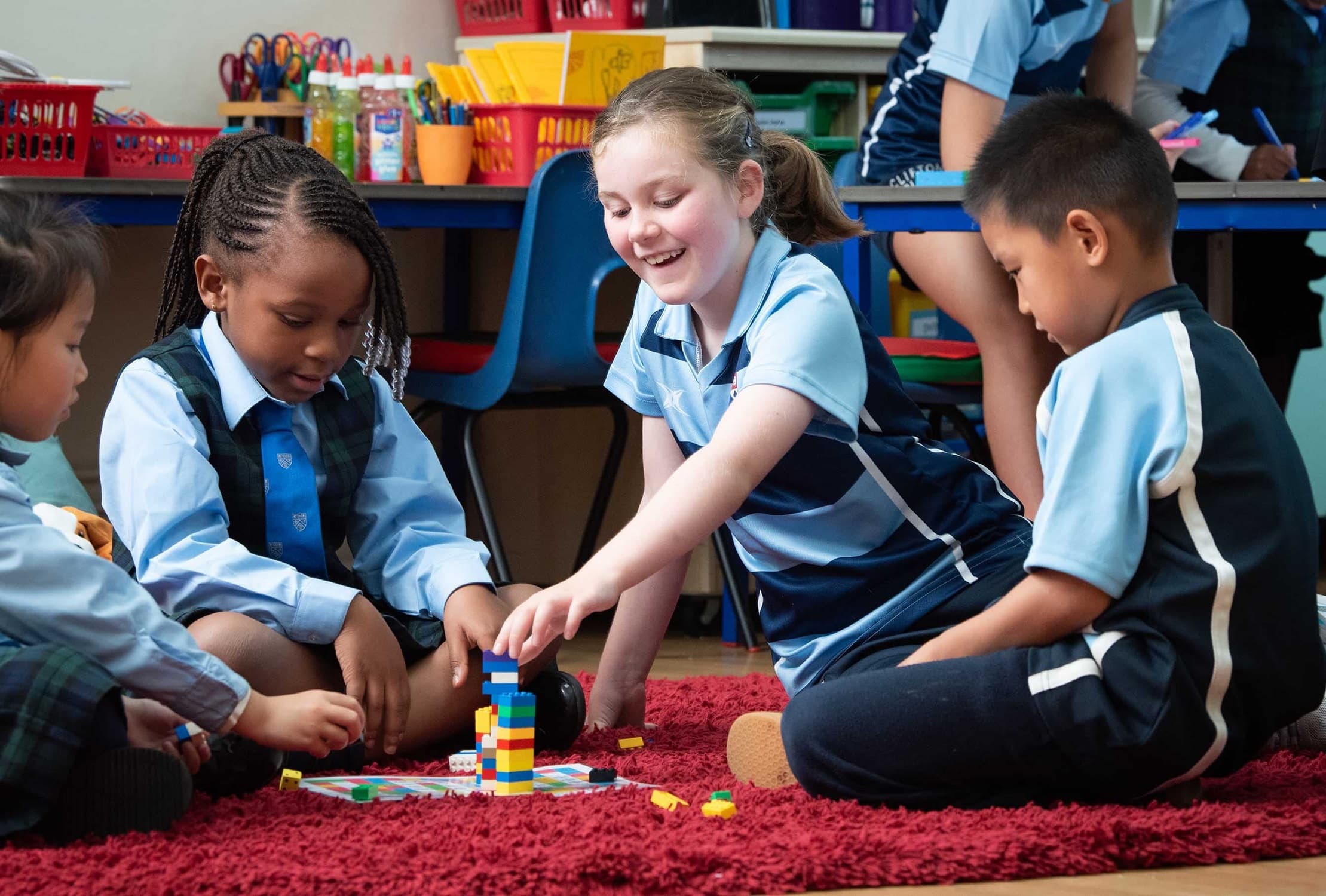 Children sitting on a red carpet, playing with colorful building blocks in a classroom setting.