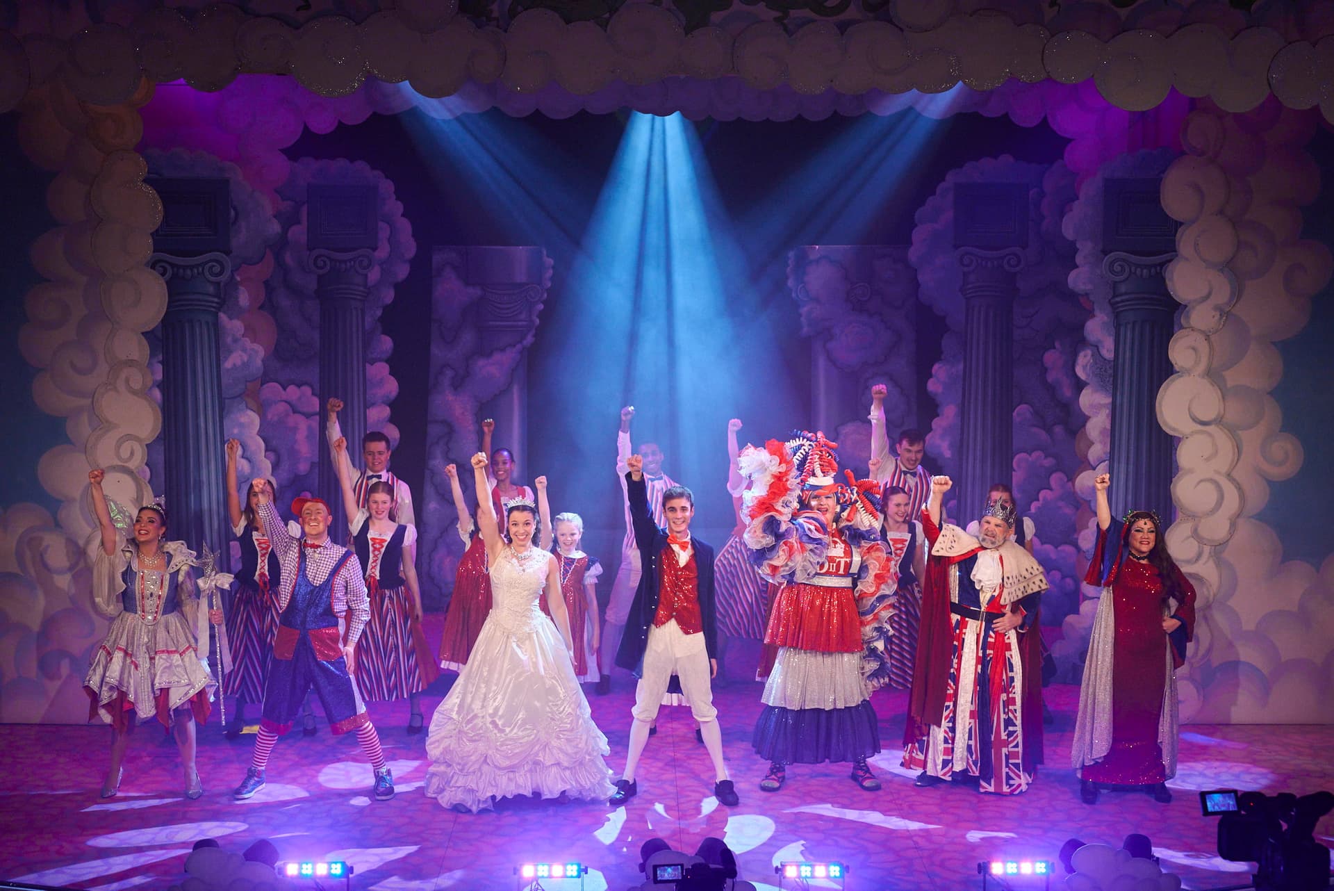 A vibrant stage performance with actors in colorful costumes striking a triumphant pose under bright spotlights and a whimsical set design.