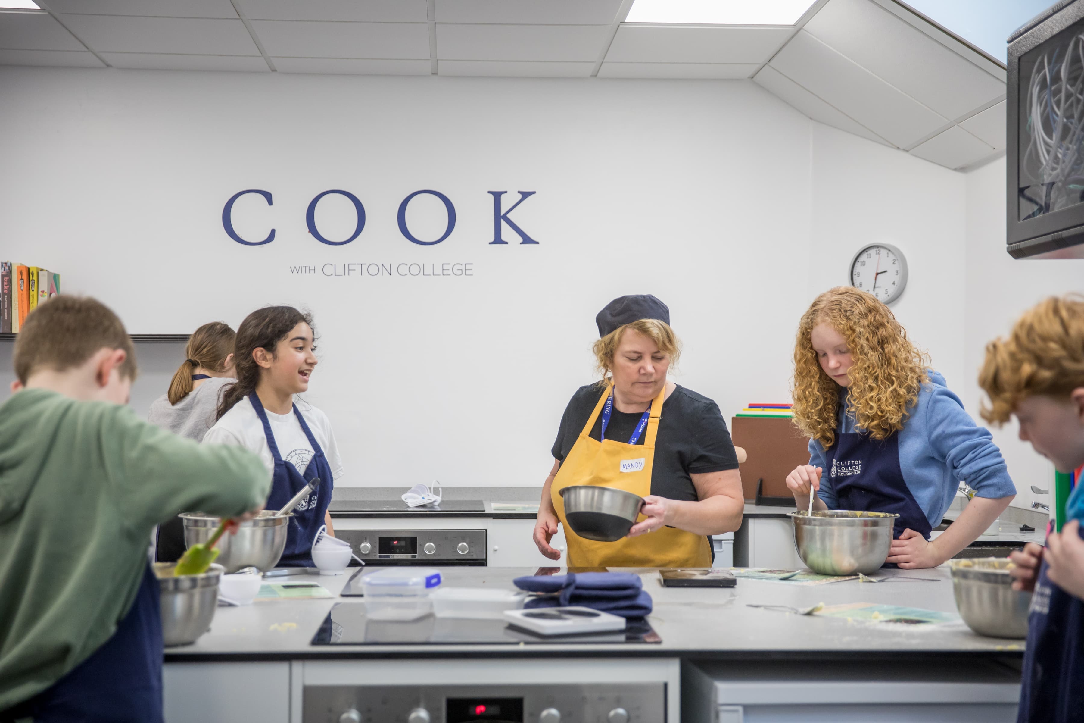 A cooking class with students and an instructor in aprons, preparing food at a kitchen counter with bowls and utensils.