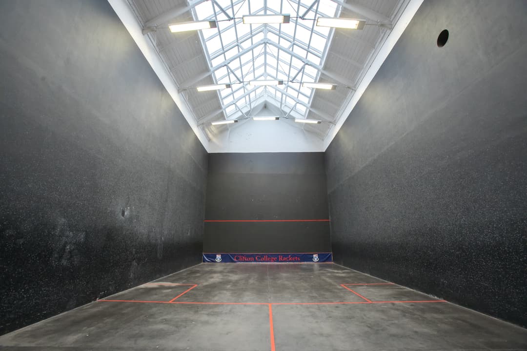 A large, empty indoor sports court with black walls, a high ceiling, and a skylight. Red lines mark the floor boundaries.