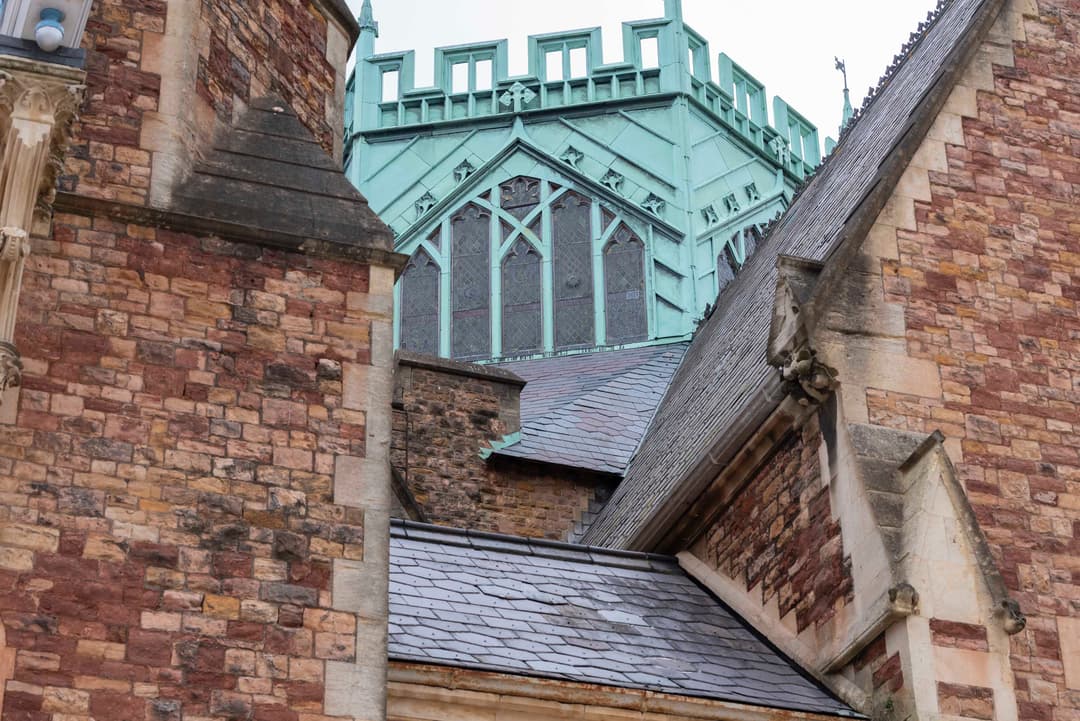 Gothic-style architecture with red brick walls, slate roofs, and a green copper tower featuring intricate window designs.