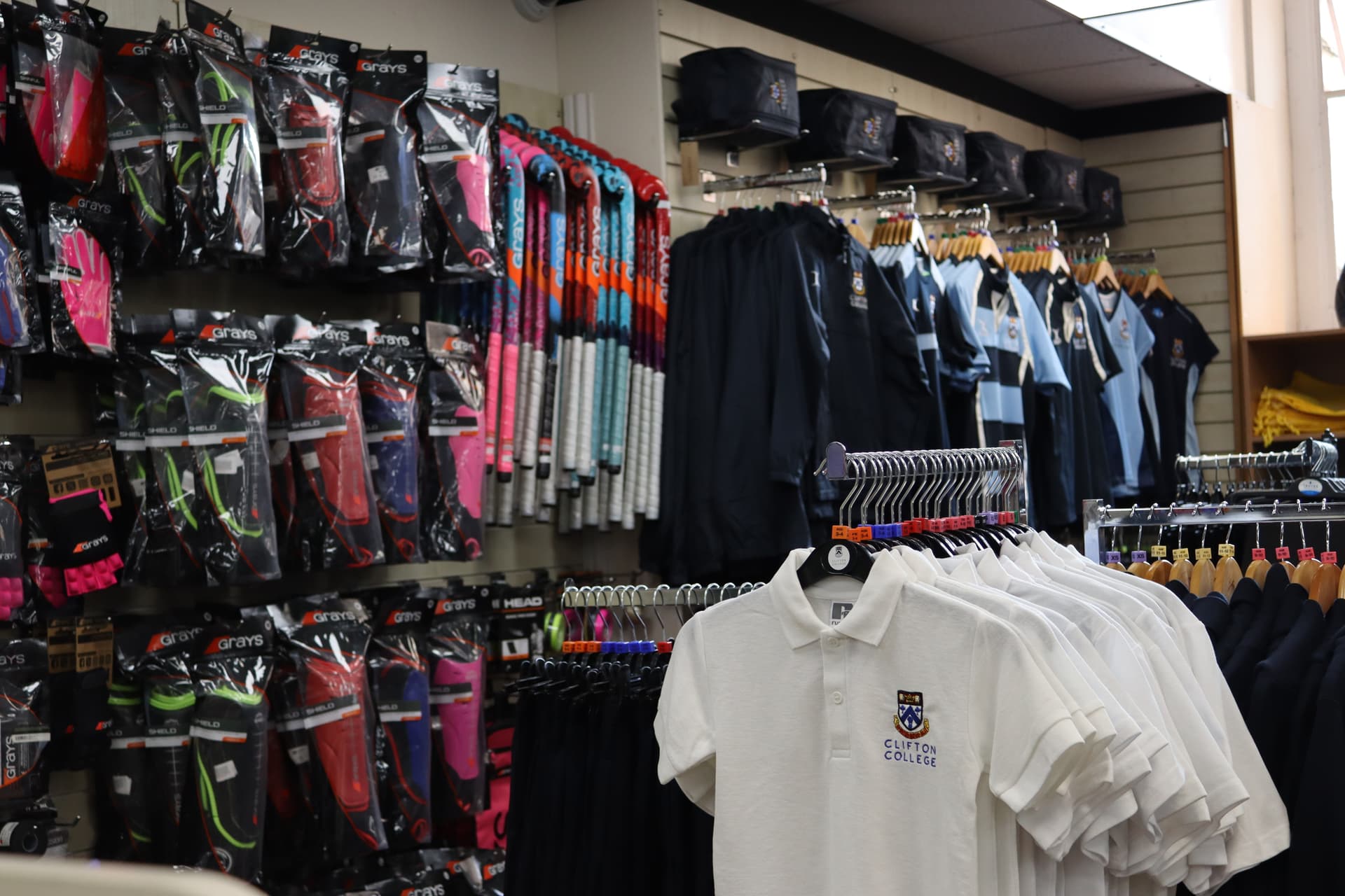 A store display with sports gear, including colorful gloves, hockey sticks, and clothing, such as white polo shirts and navy jackets.