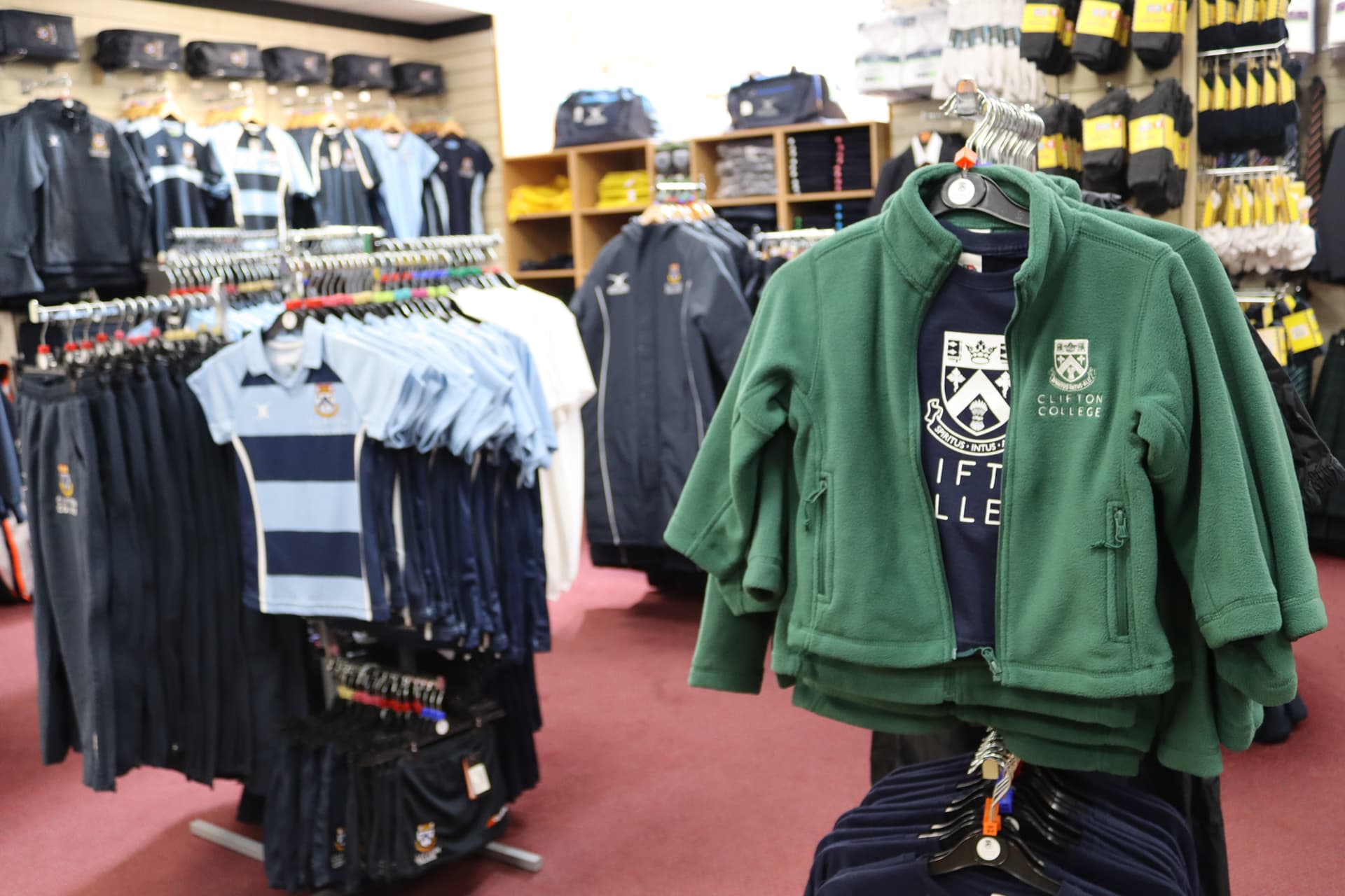 School uniforms displayed in a store, featuring green jackets, striped shirts, and various clothing items on racks.