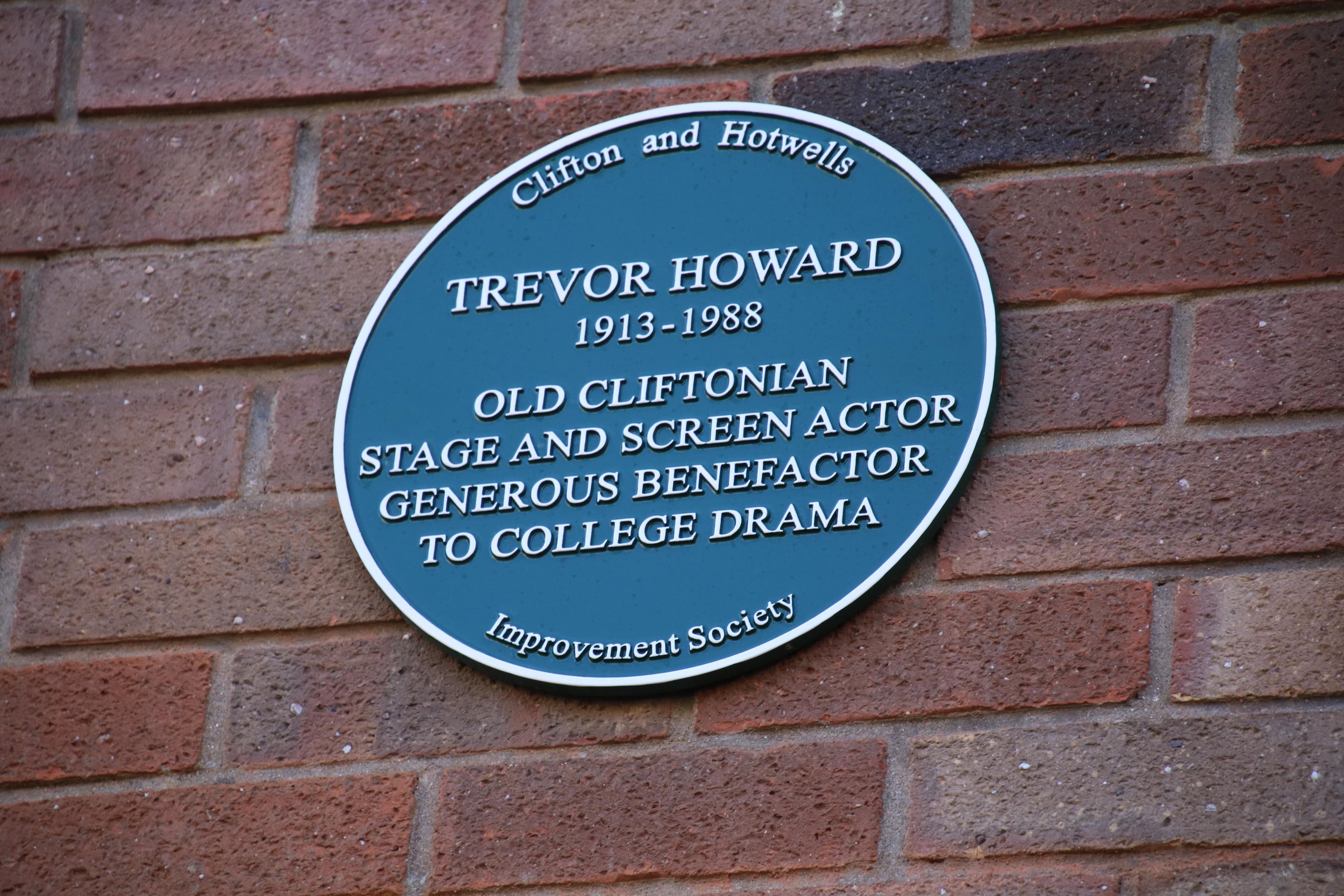 Green plaque on brick wall honouring Trevor Howard, 1913-1988, as a stage and screen actor and benefactor to college drama.