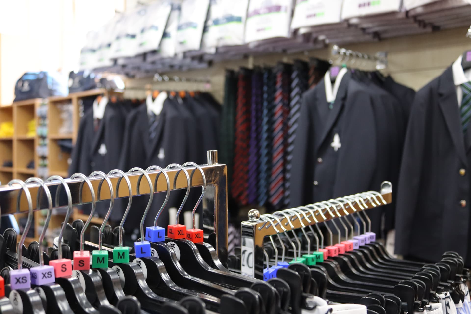 A clothing store displays school uniforms, including blazers, ties, and shirts, neatly arranged on racks with size labels.