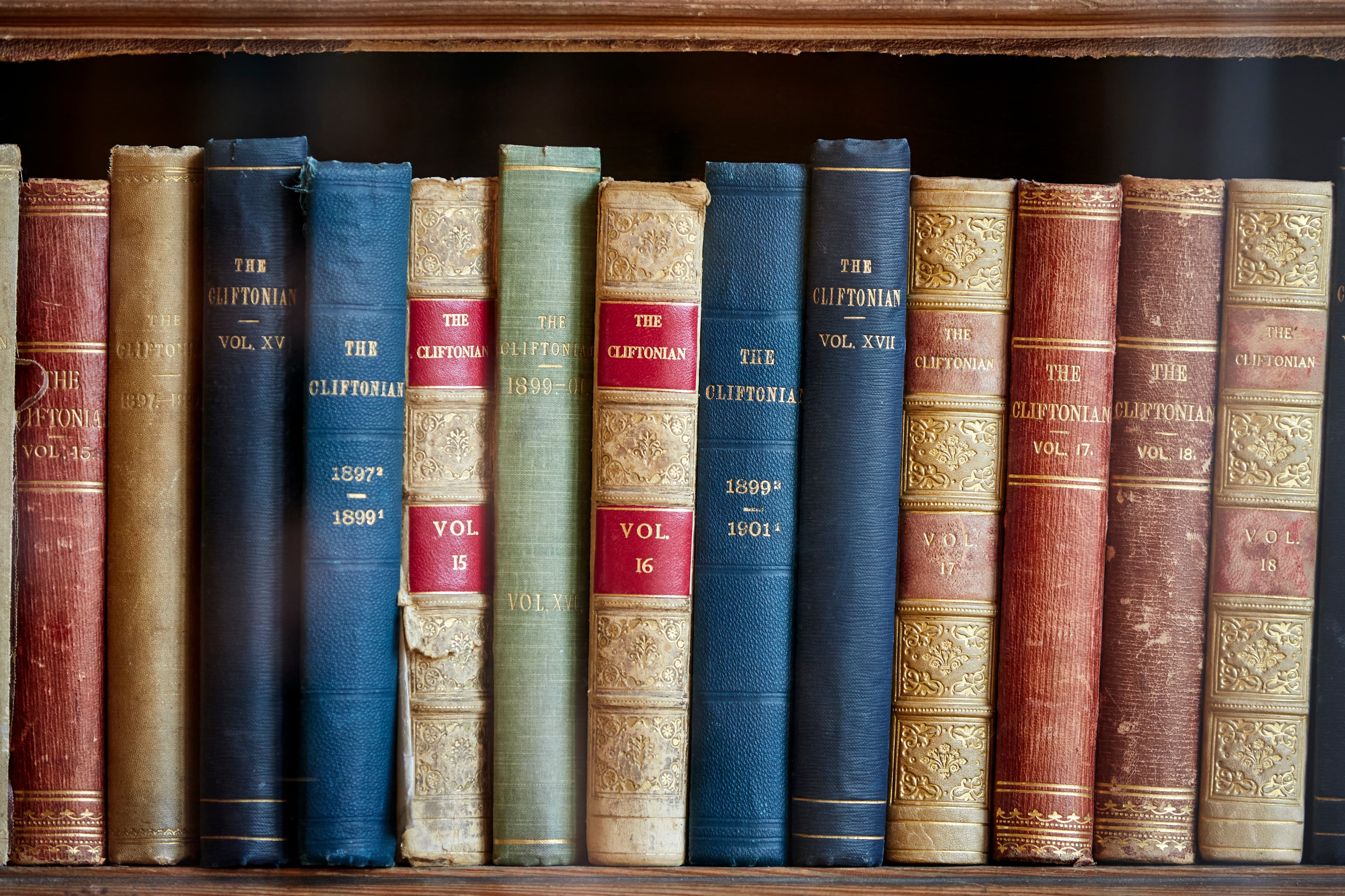 A row of vintage books with varied colors and volumes, titled "The Cliftonian," displayed on a wooden shelf.
