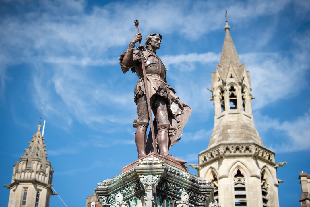 Bronze statue of a historical figure holding a staff, with ornate church spires and a blue sky in the background.