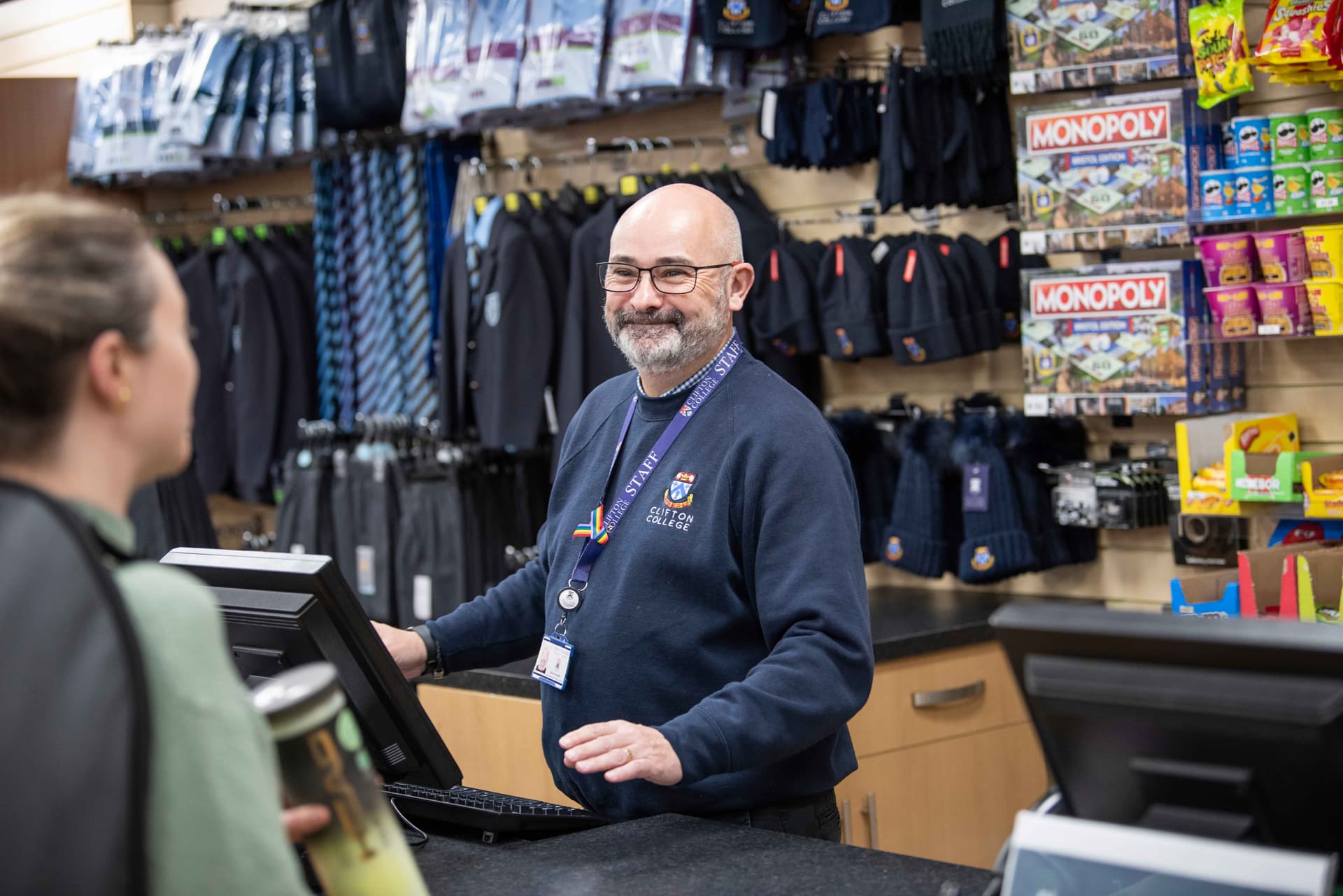 A man in the school shop serving a woman behind the till