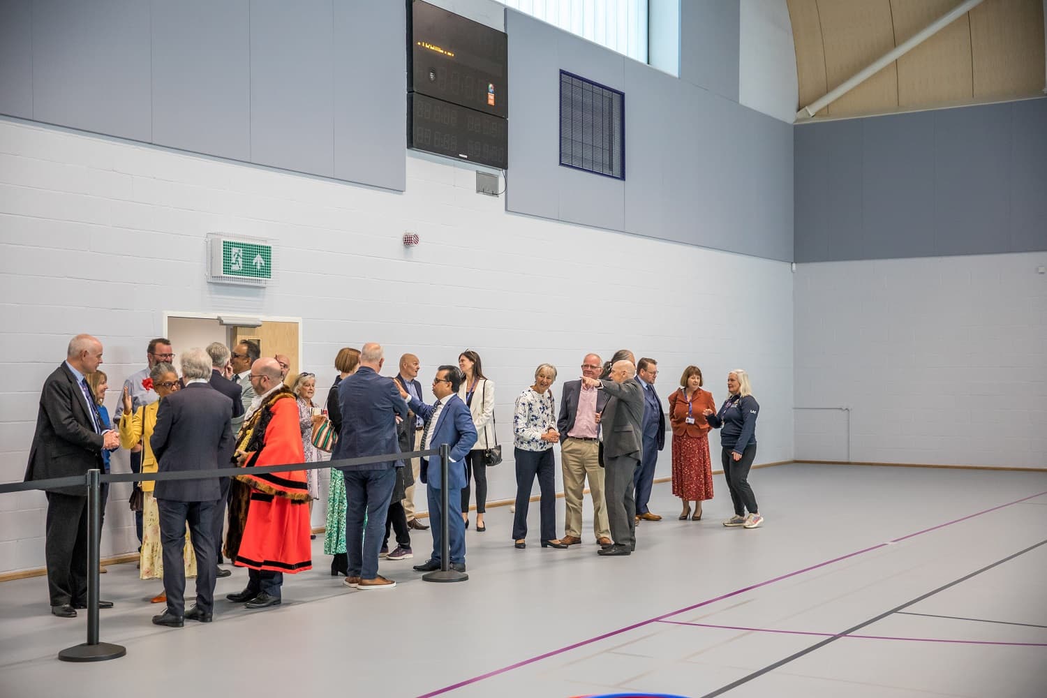A group of people, including some in ceremonial attire, stand in line inside a large, modern hall with high ceilings and light-colored walls.