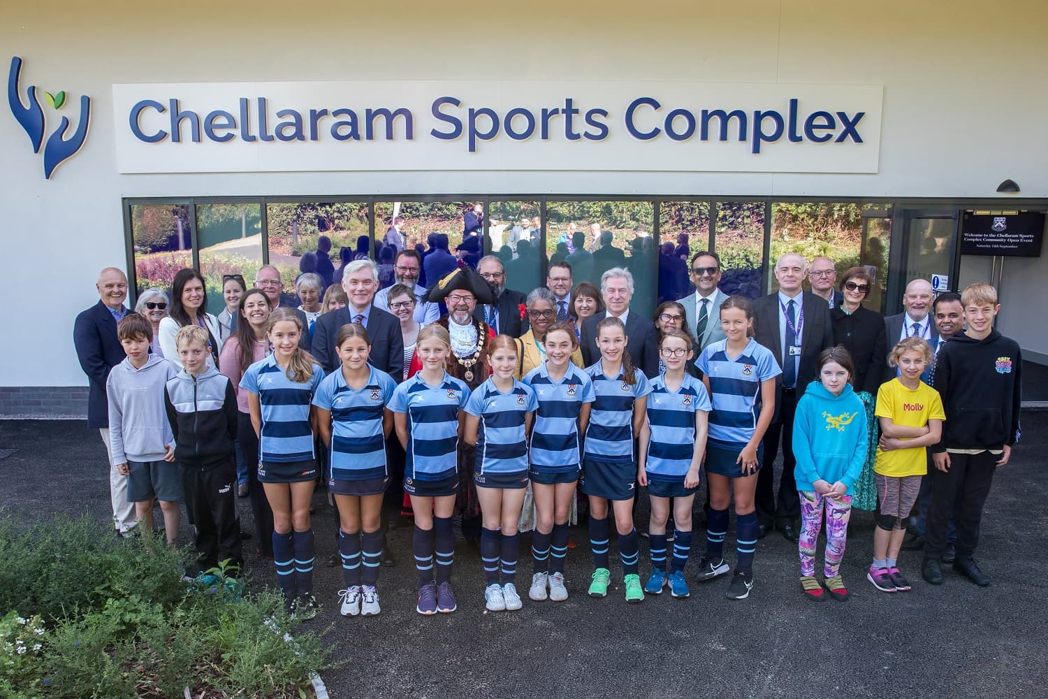 A group of people, including children in sports uniforms, pose in front of the Chellaram Sports Complex building.
