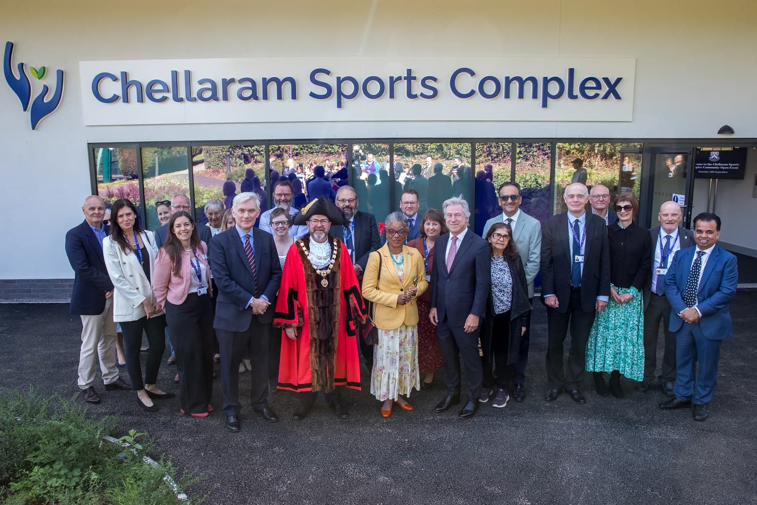 A group of people, including a person in ceremonial attire, stand in front of the Chellaram Sports Complex building.