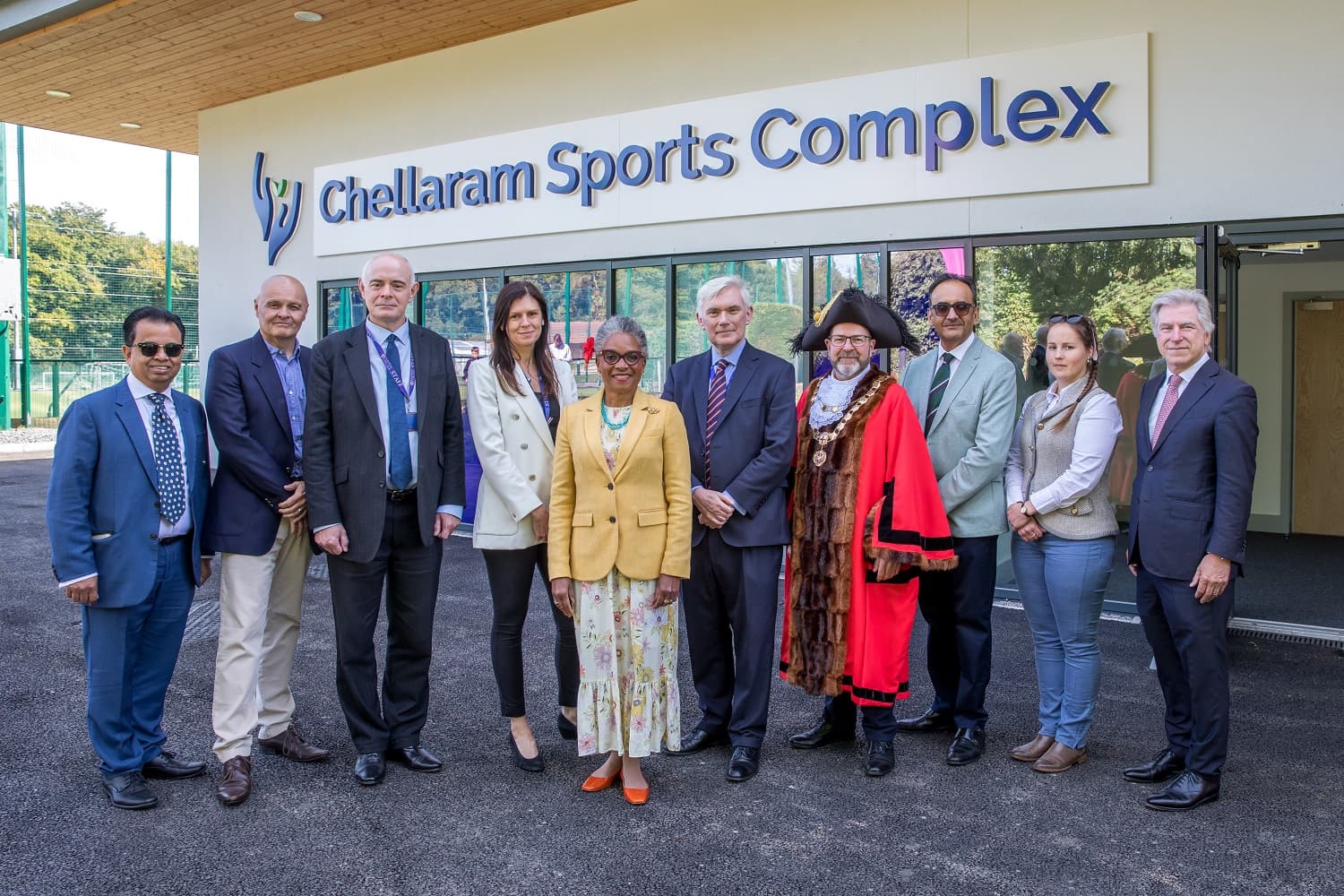 A group of people, including a person in ceremonial attire, stand in front of the Chellaram Sports Complex building.